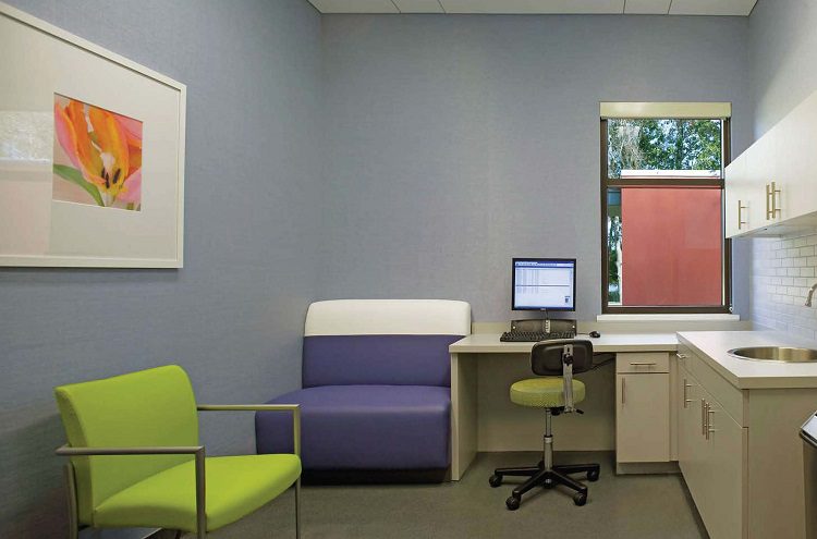 A medical office with a desk, chair and sink.