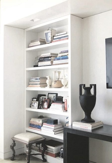 A white shelf with books and a vase on it.