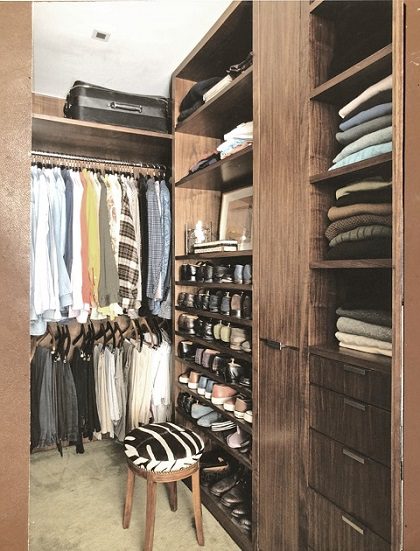 A walk in closet with clothes and a stool.