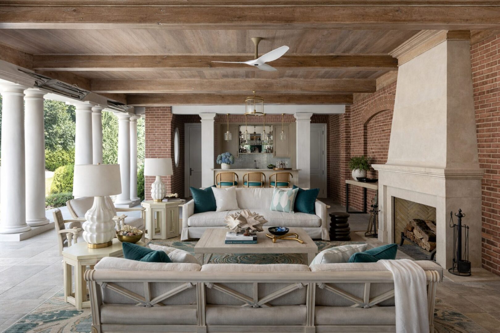 Neo-classical Southampton poolhouse interior with brick fireplace, coffered wood ceiling, and open-air colonnade
